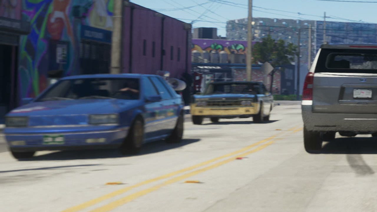 Blue sedan driving down a mural-lined Stockyard street, in GTA VI Trailer 1