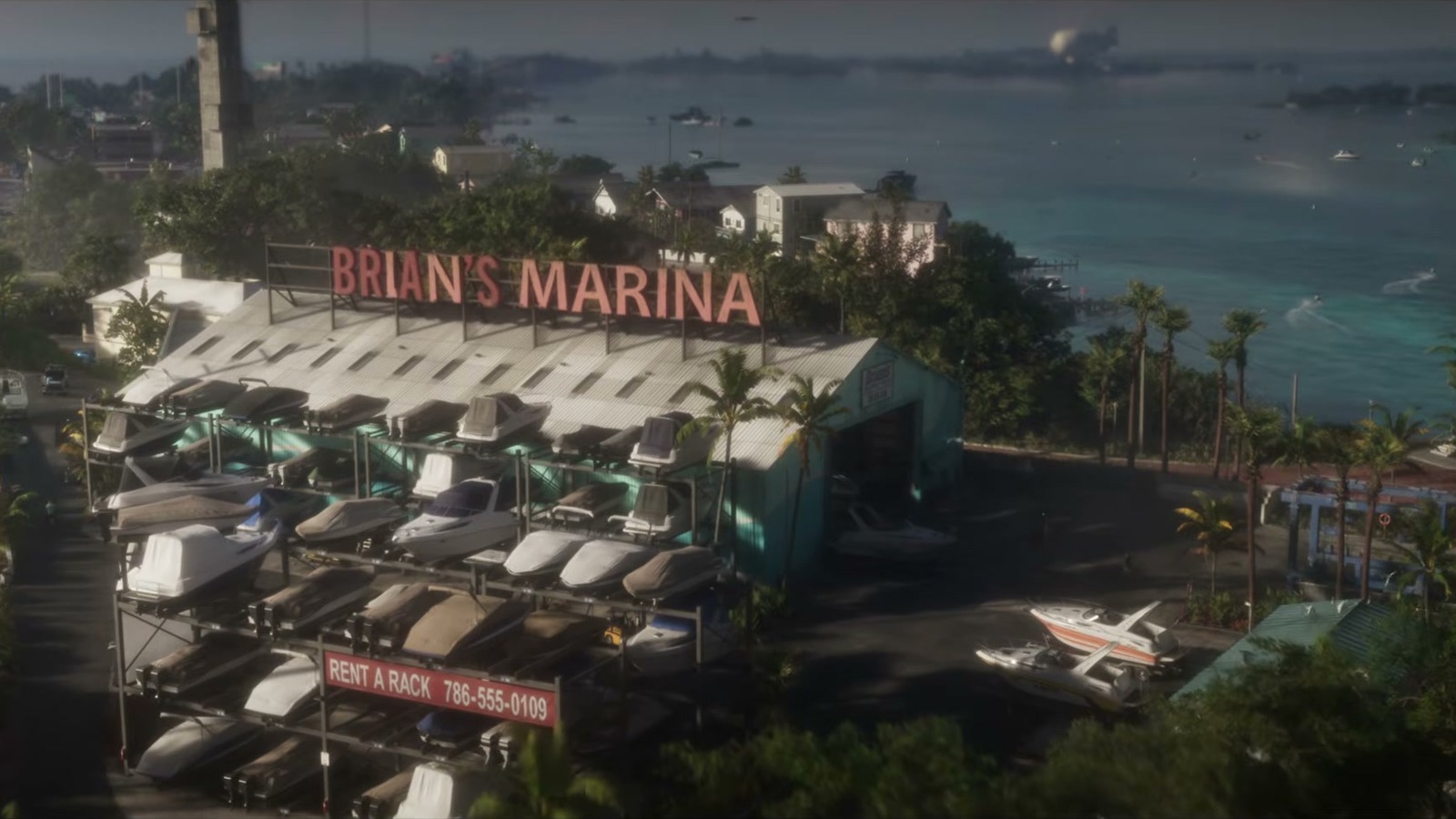 Aerial view of a boat storage building with a large red Brian's Marina sign, turquoise water and houses behind.