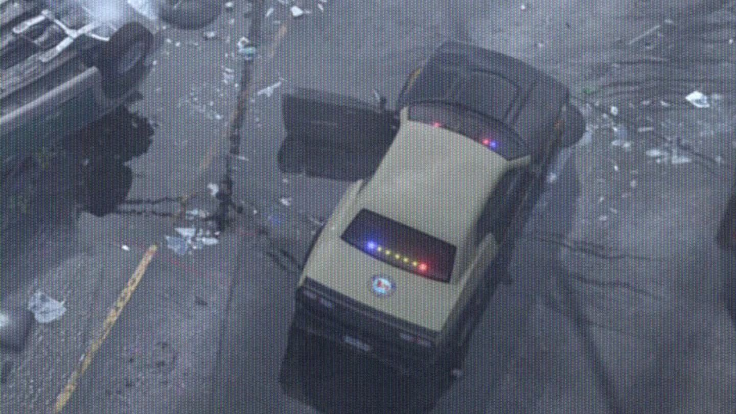 Beige muscle-car patrol unit with its lights on next to a highway crash, seen from a helicopter, in GTA VI Trailer 1