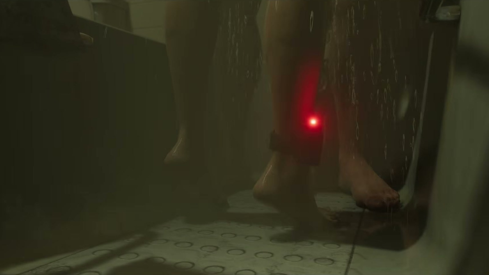 Wet legs in a shower; on one ankle, an electronic monitor with a red light.