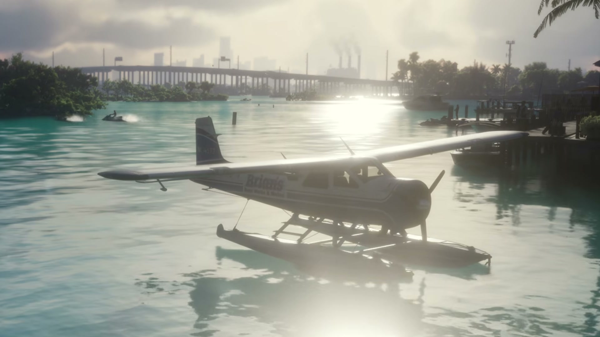 White high-wing seaplane on floats moored by the dock, with a bridge and the city behind