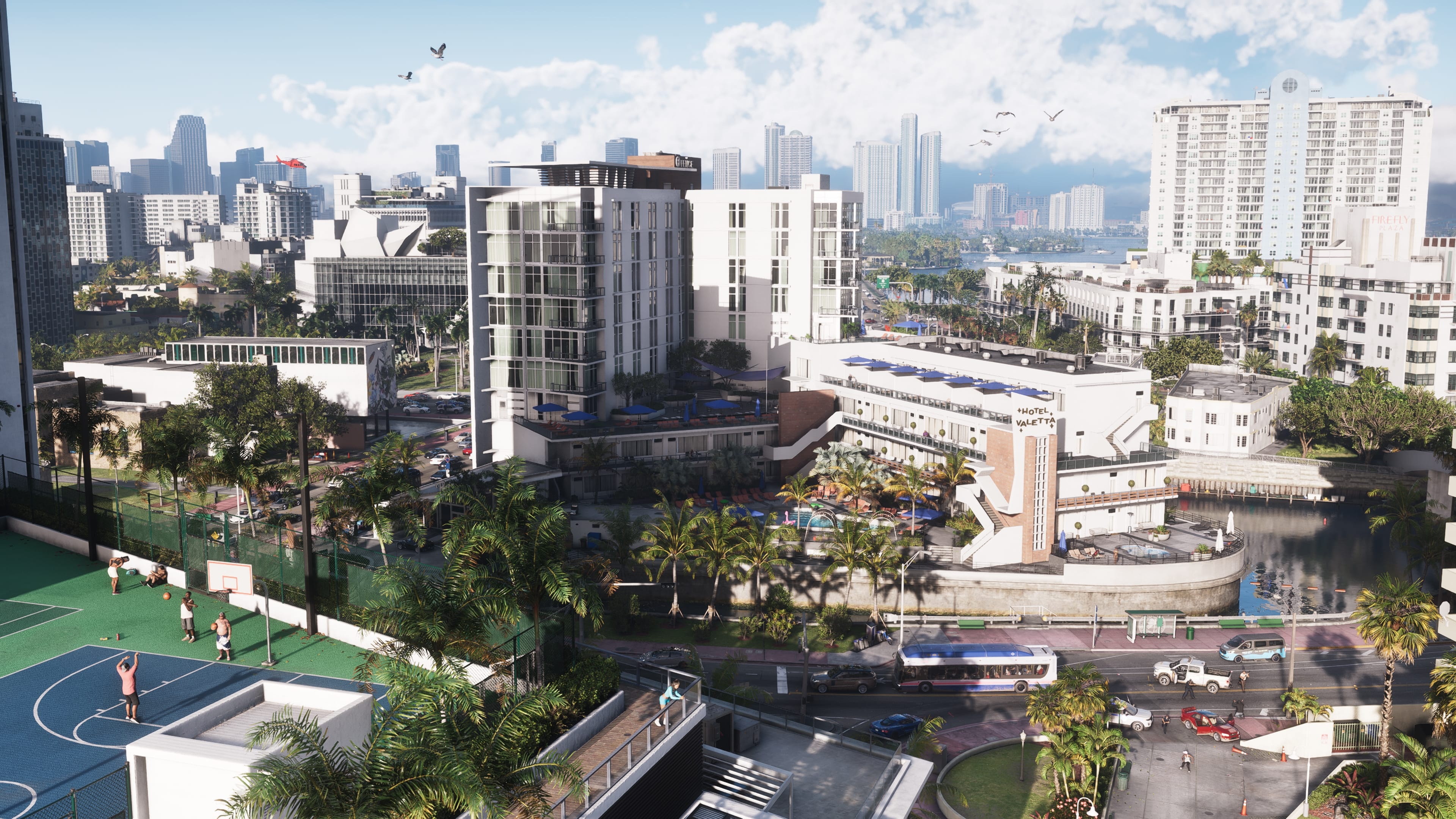 Elevated view of downtown with white buildings, a basketball court and palm trees, by day.