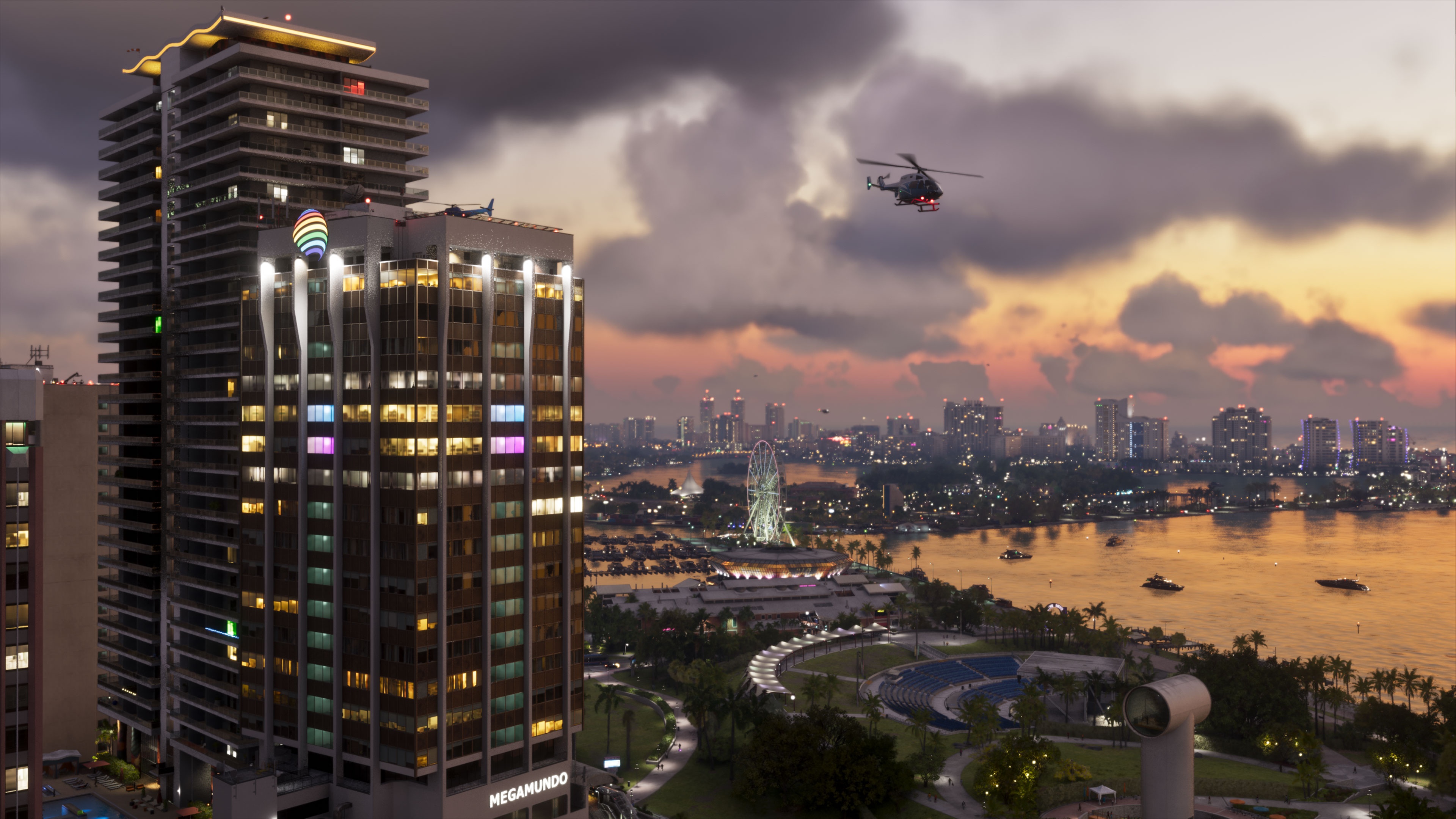 Lit skyscrapers by the bay at sunset, with a helicopter in the sky.