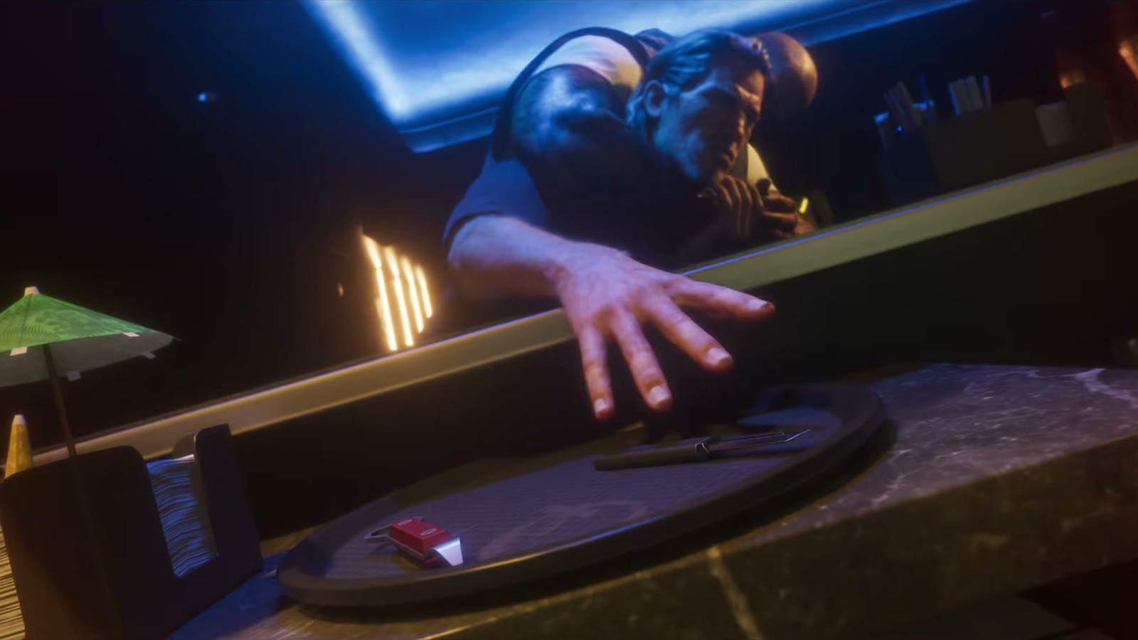 A man sprawled across a blue-lit bar with a cocktail umbrella in front.