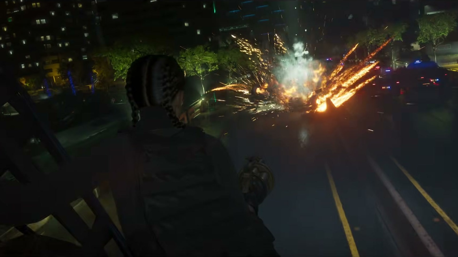 A person seen from behind facing a sparking explosion on a night road.