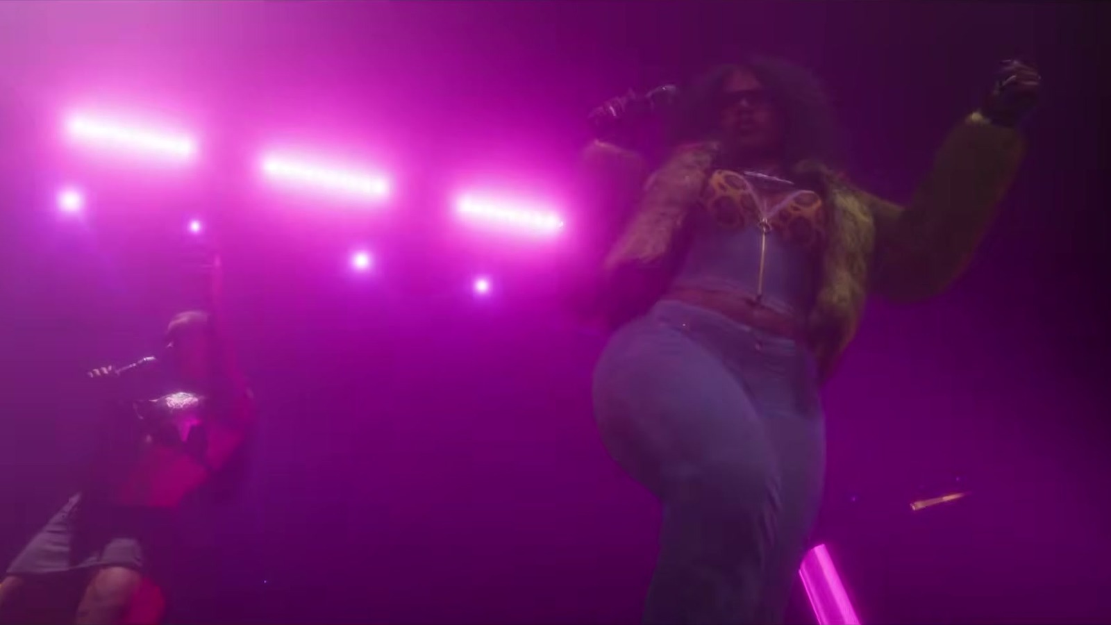 A woman in a corset and fur jacket dances in a magenta-lit club.