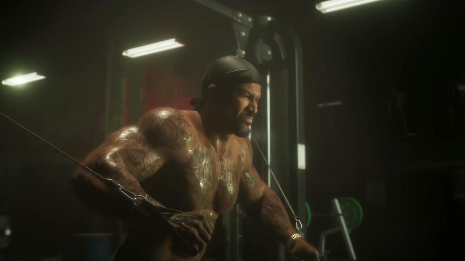 A tattooed shirtless man works a cable machine in a dark gym.