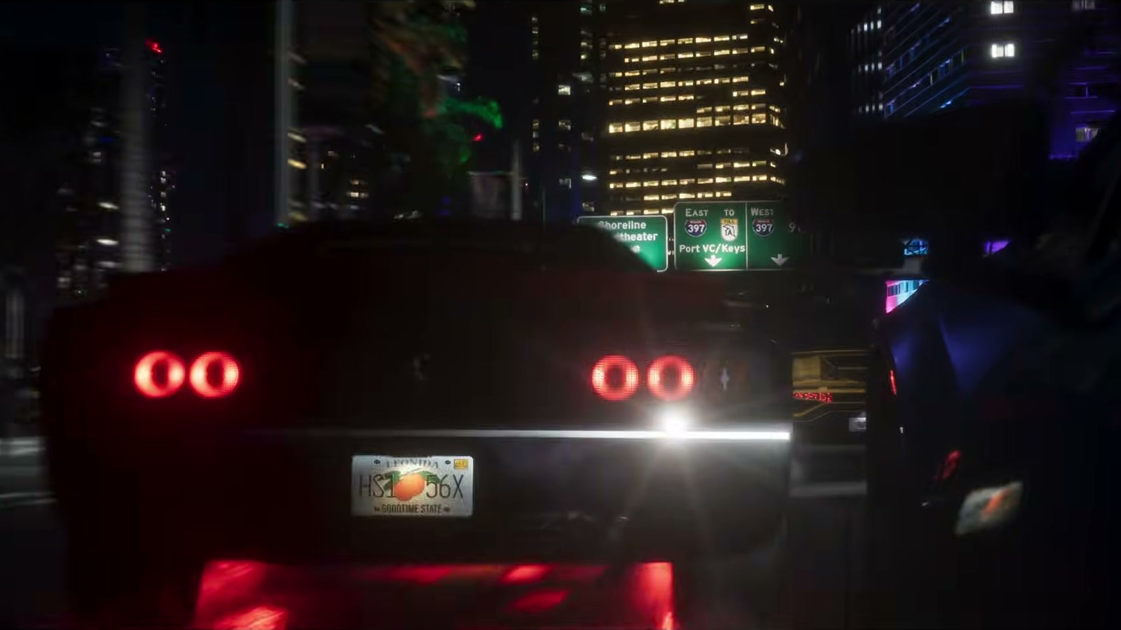 Night street race seen behind a muscle car with round tail-lights, under green highway signs.