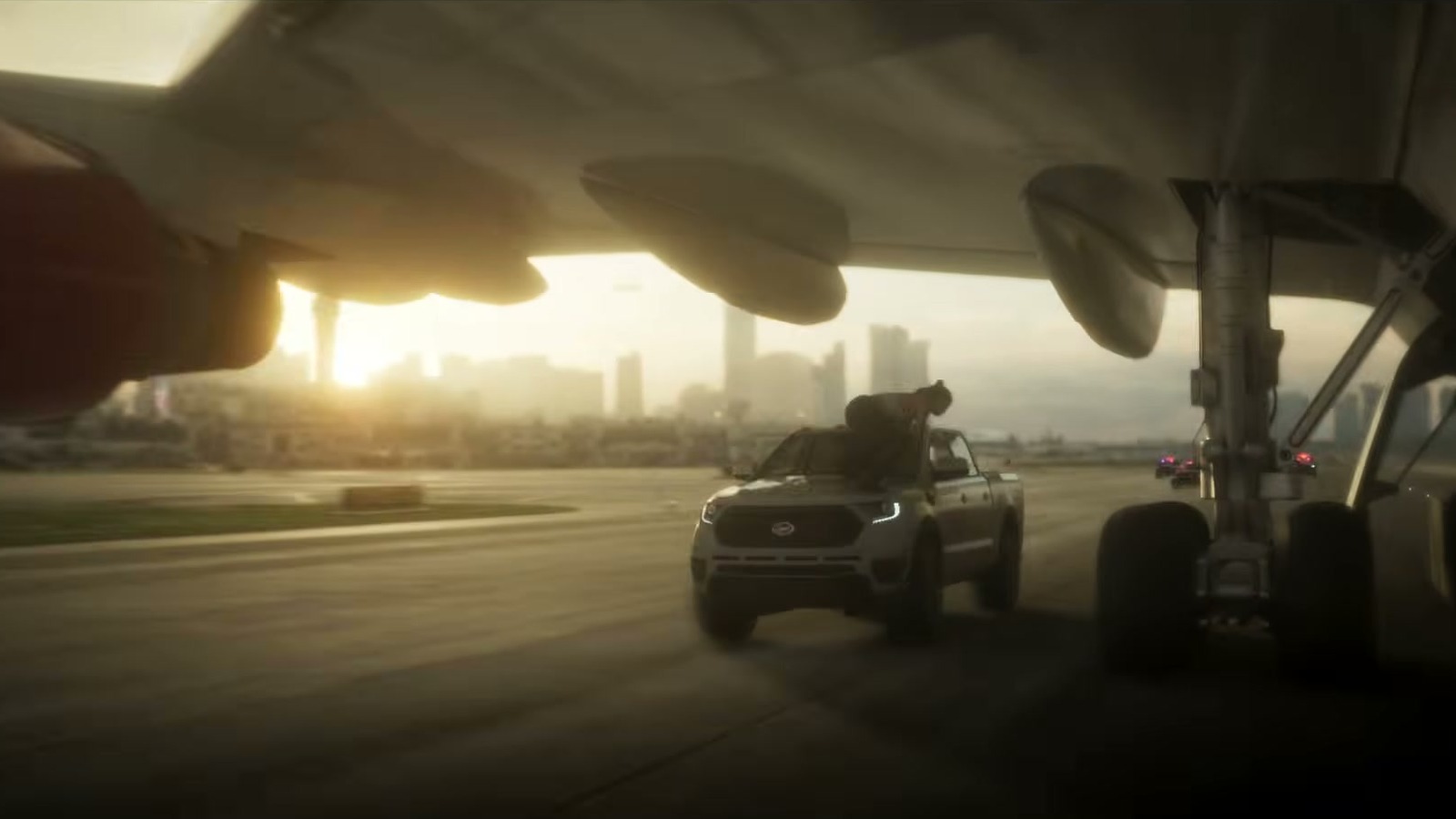 A pickup races down a runway under a plane's landing gear, with towers in the distance.