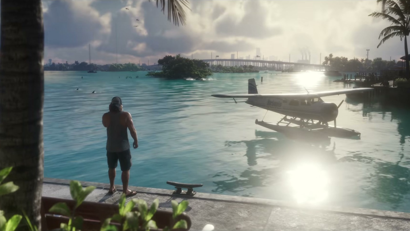 A man seen from behind on a seawall beside a white floatplane in turquoise water, a bridge in the distance.