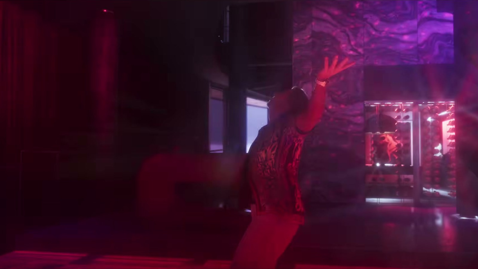 A man in a patterned shirt arches back, one arm raised, in a magenta-lit club.