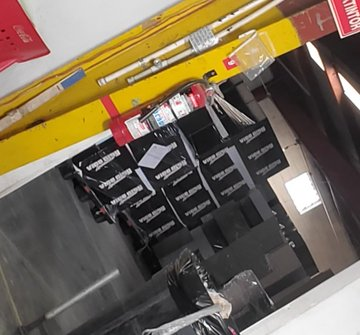 Apilado de cajas negras en un almacén, con texto blanco en las tapas. Foto no verificada.